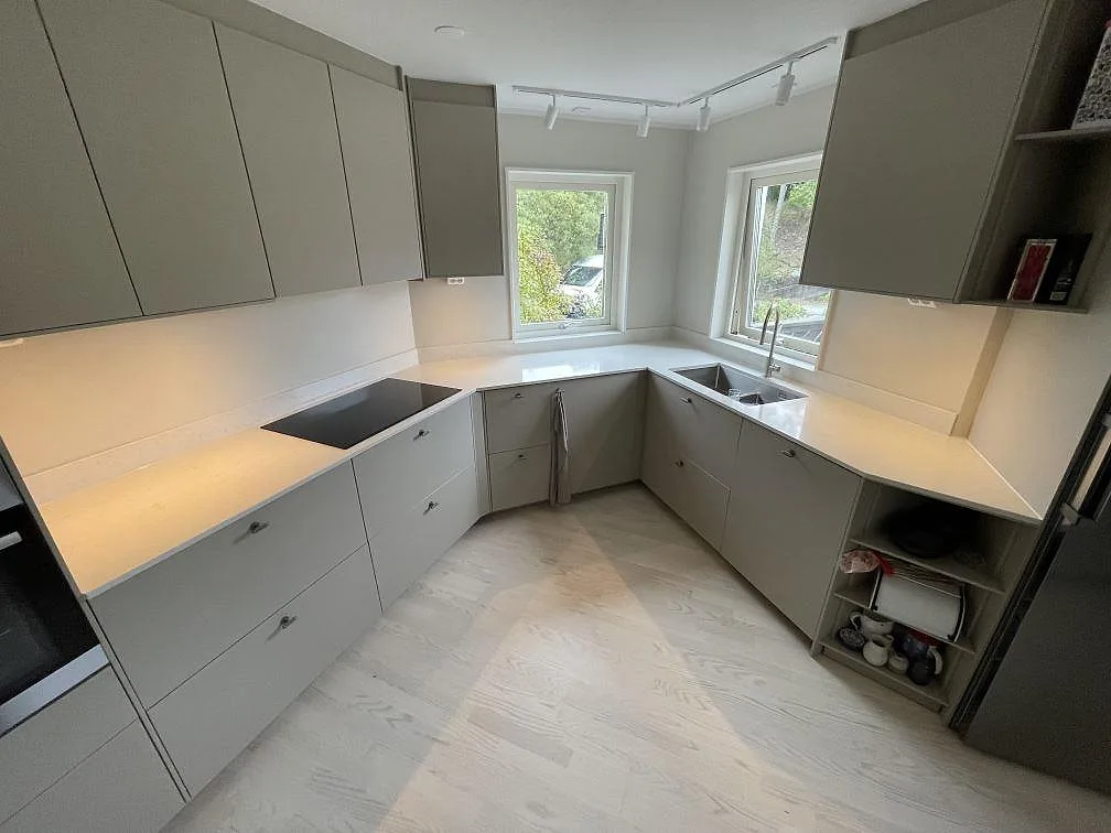 Köksbänkskiva i Silestone Snowy Ibiza, polerad kvartskomposit, i ett L-format kök i Älta med hällzon, diskho och låg stänkkant.