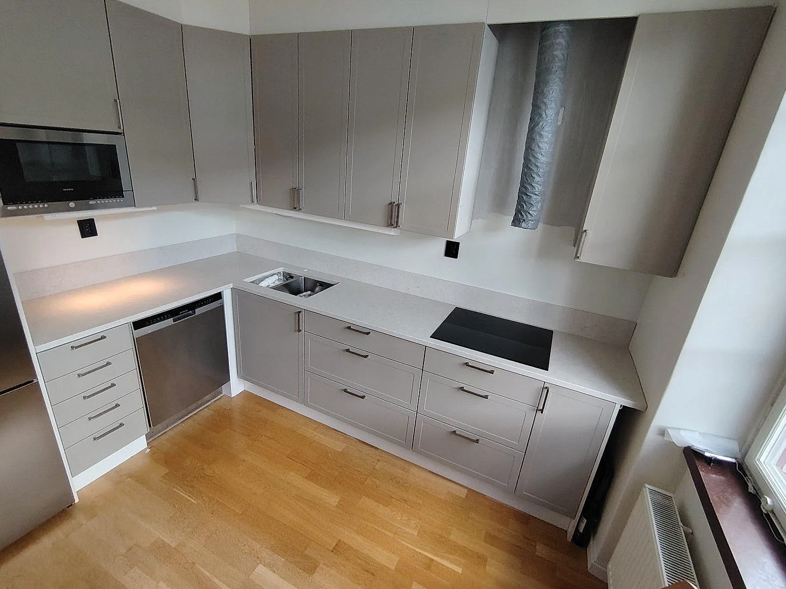 L-format kök i Älvsjö med polerad Silestone Snowy Ibiza komposit som bänkskiva, stänkskydd, svart induktionshäll och rostfri diskho.