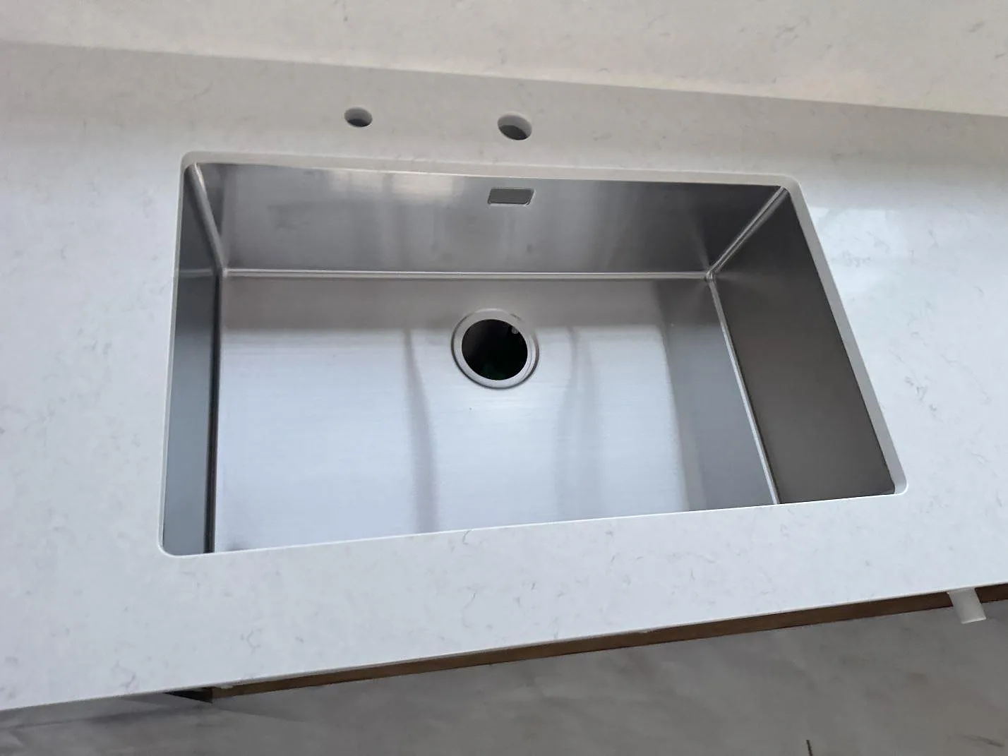 Detaljbild av rostfri diskho infälld i ljus polerad Silestone Snowy Ibiza kvartskomposit i kök i Alvesta.