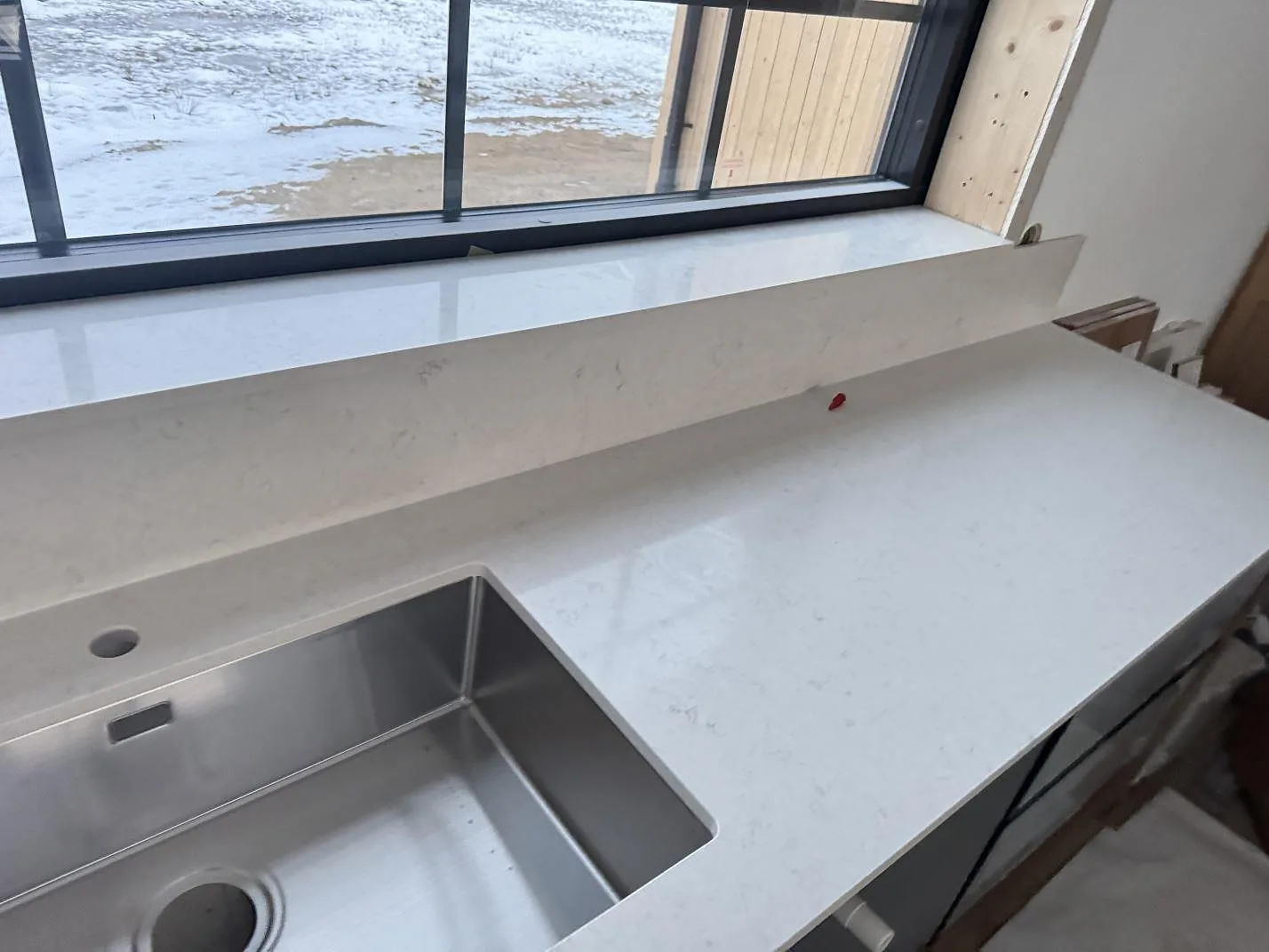 Höger sida av köksbänkskiva i polerad Silestone Snowy Ibiza med stänkkant och synlig grå ådring i Alvesta.