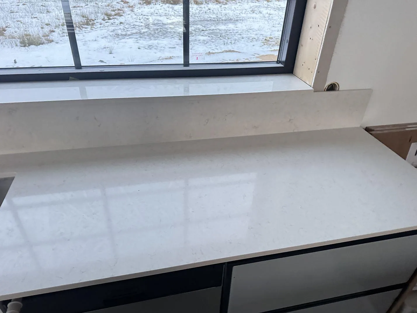 Polerad Silestone Snowy Ibiza arbetsyta med matchande stänkkant under ett fönster i ett kök i Alvesta.