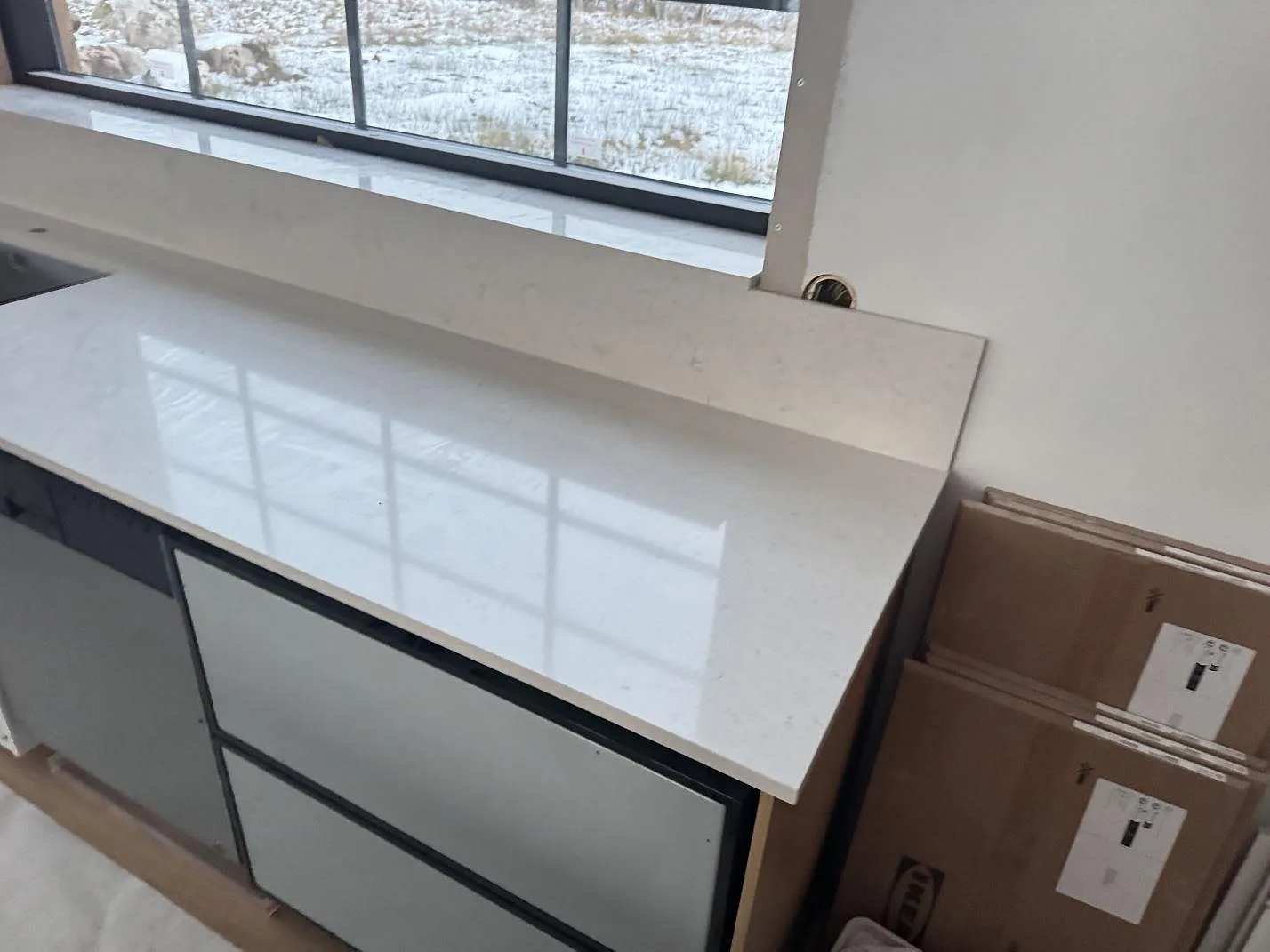 Ändvy av ljus Silestone Snowy Ibiza bänkskiva, polerad, med stänkkant och träinredning under montering i Alvesta.
