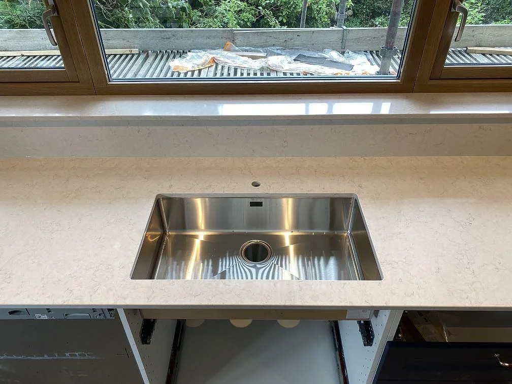 Närbild på rostfri diskho i en polerad köksbänkskiva av Silestone Snowy Ibiza med 12 mm stänkkant vid fönster i Arlöv.