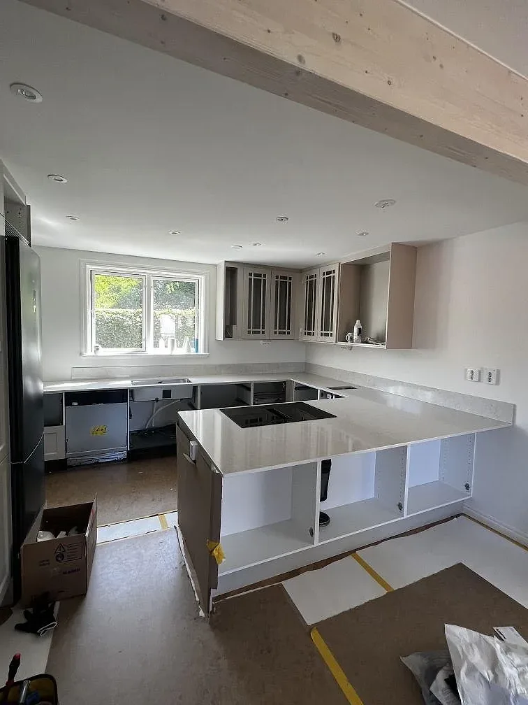 Köksbänkskiva i polerad Silestone Snowy Ibiza med svart induktionshäll, uppvikt stänkkant och stora fönster i ett kök i Båstad.
