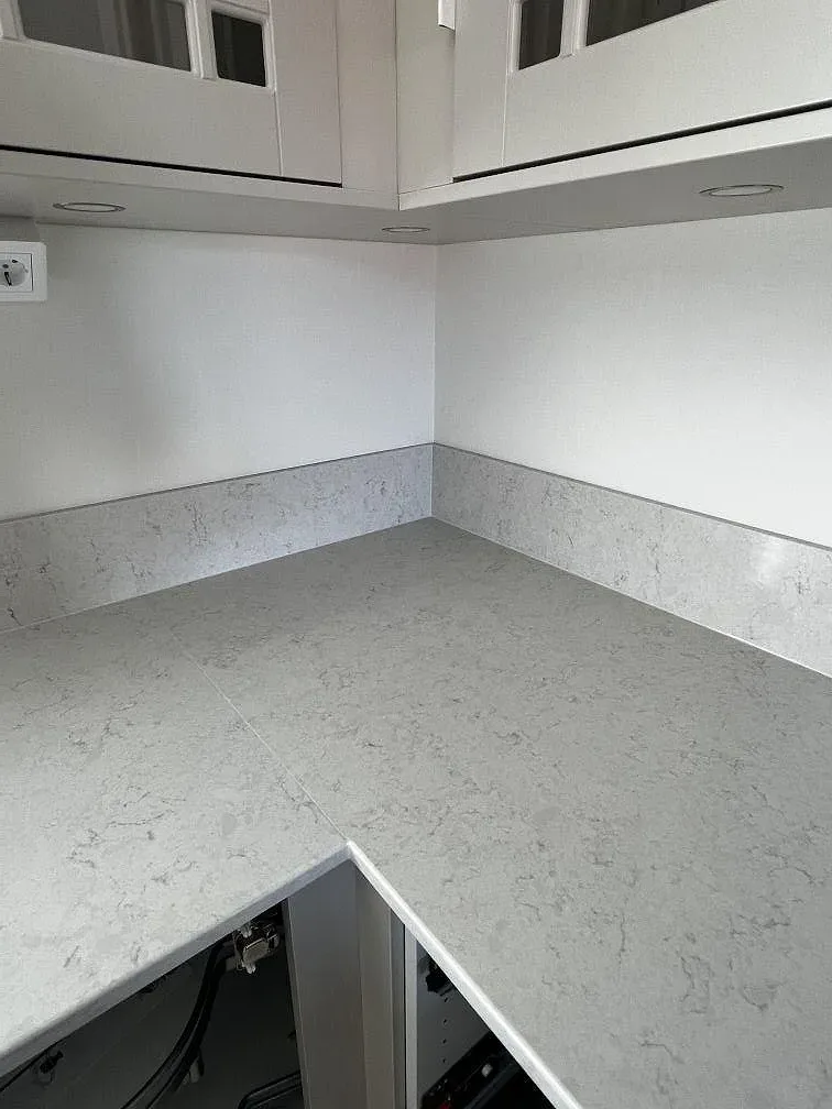 Detalj av polerad Silestone Snowy Ibiza med matchande uppvikt stänkkant och ljus grå ådring i kök i Båstad.