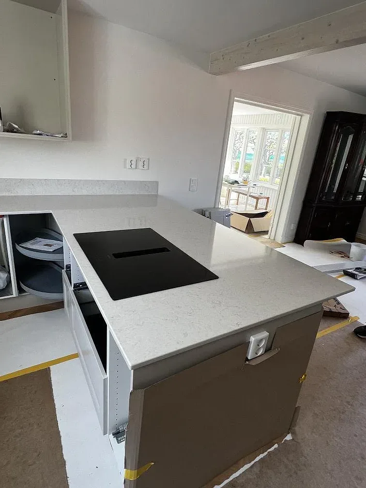Närbild av köksö med polerad Silestone Snowy Ibiza, svart häll och ljus kompositsten i ett kök under montering i Båstad.