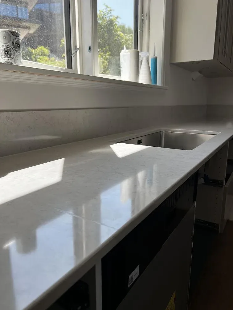 Polerad Silestone Snowy Ibiza som köksbänkskiva med diskho, häll och reflektioner från stora fönster i Båstad.