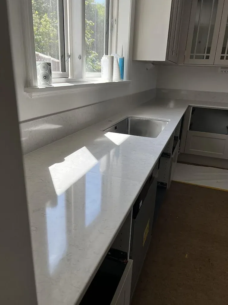 Lång köksbänkskiva i polerad Silestone Snowy Ibiza med diskho, häll och fönsterljus i Båstad.