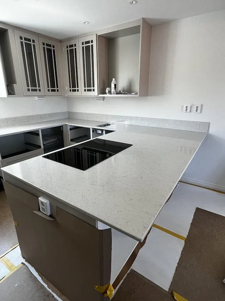 Polerad köksbänkskiva i Silestone Snowy Ibiza med svart induktionshäll på köksö och vit skåpinredning i Båstad.