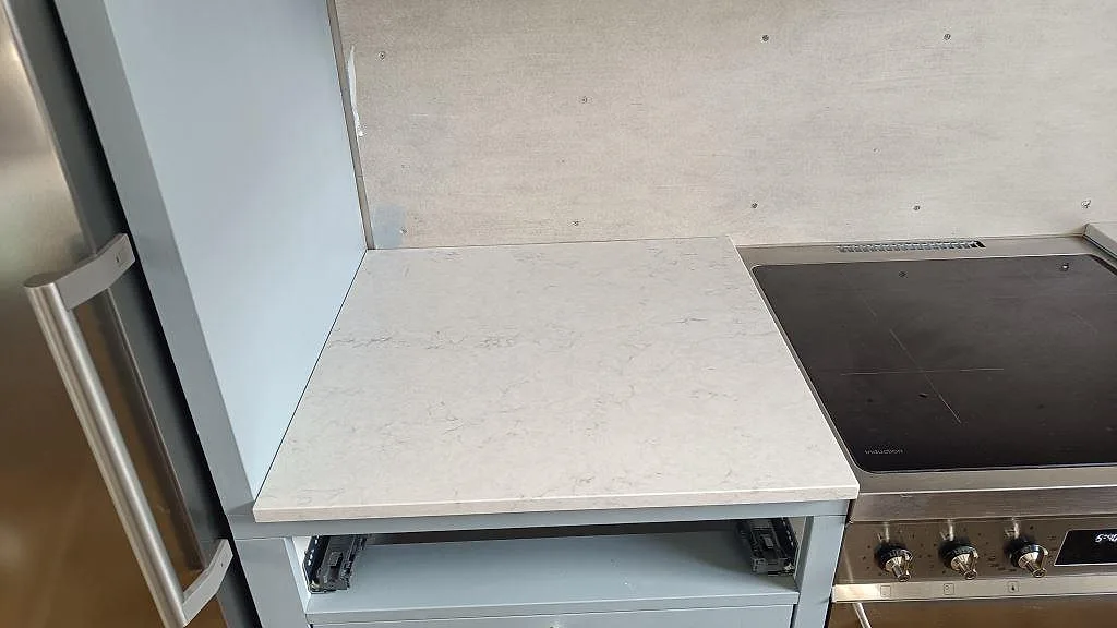 Detalj av 20 mm bänkskiva i polerad Silestone Snowy Ibiza, vit kvartskomposit med ljus grå ådring bredvid spisen i Båstad.