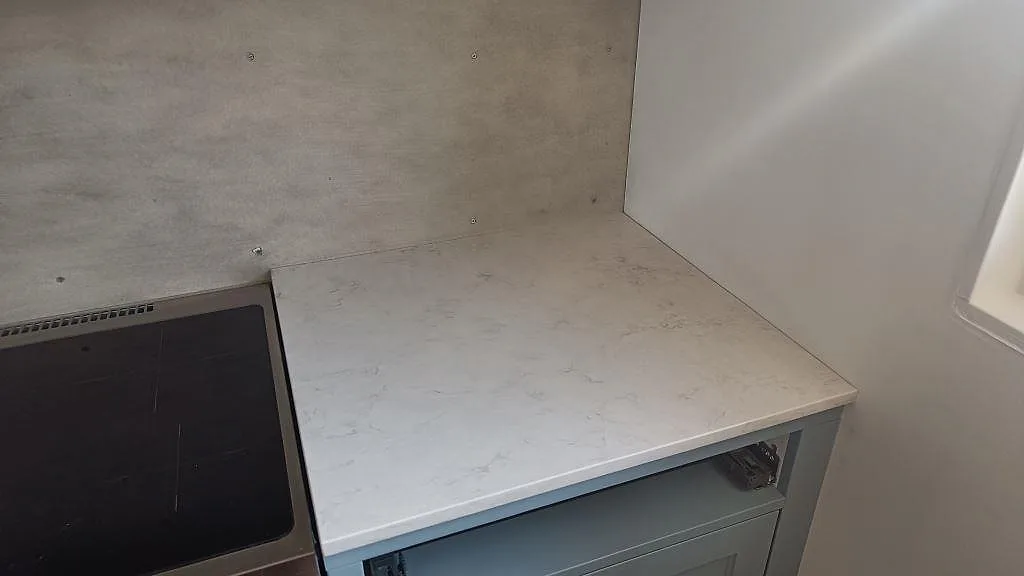 Hörndetalj av polerad Silestone Snowy Ibiza, vit kvartskomposit på bänkraden vid spisen och väggen i ett kök i Båstad.