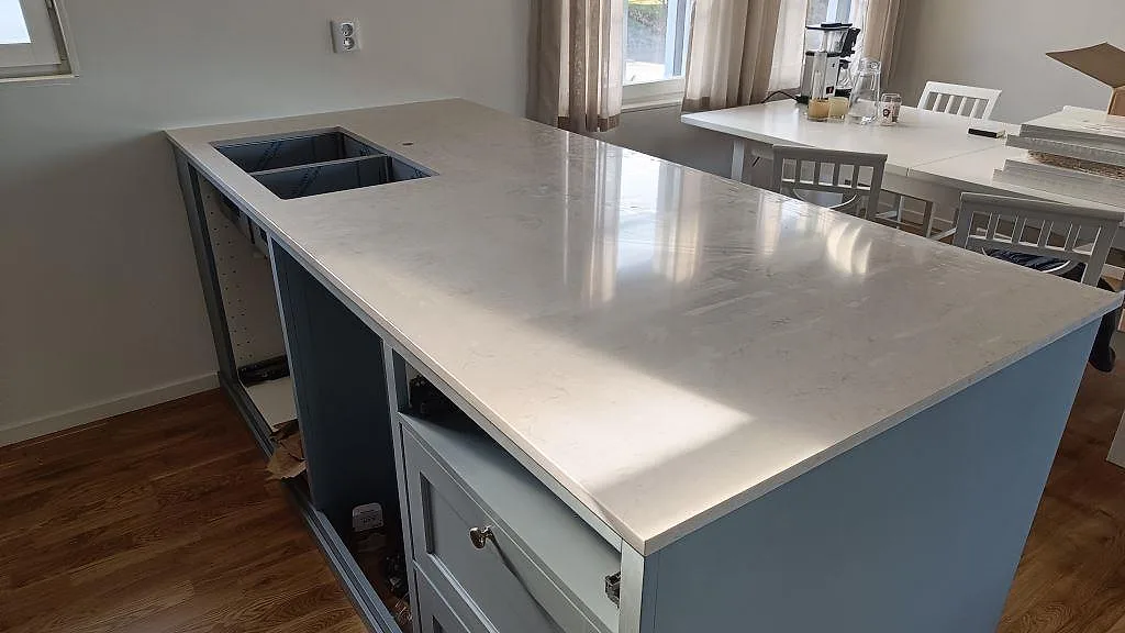 Stor köksö i polerad Silestone Snowy Ibiza, vit kvartskomposit med synlig diskhoöppning och ljus ådring i Båstad.