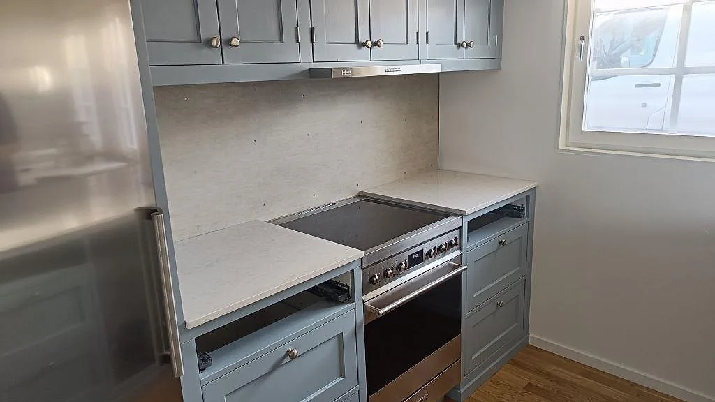 Bänkskivor i polerad Silestone Snowy Ibiza, vit kvartskomposit runt en fristående spis med väggyta bakom i ett kök i Båstad.
