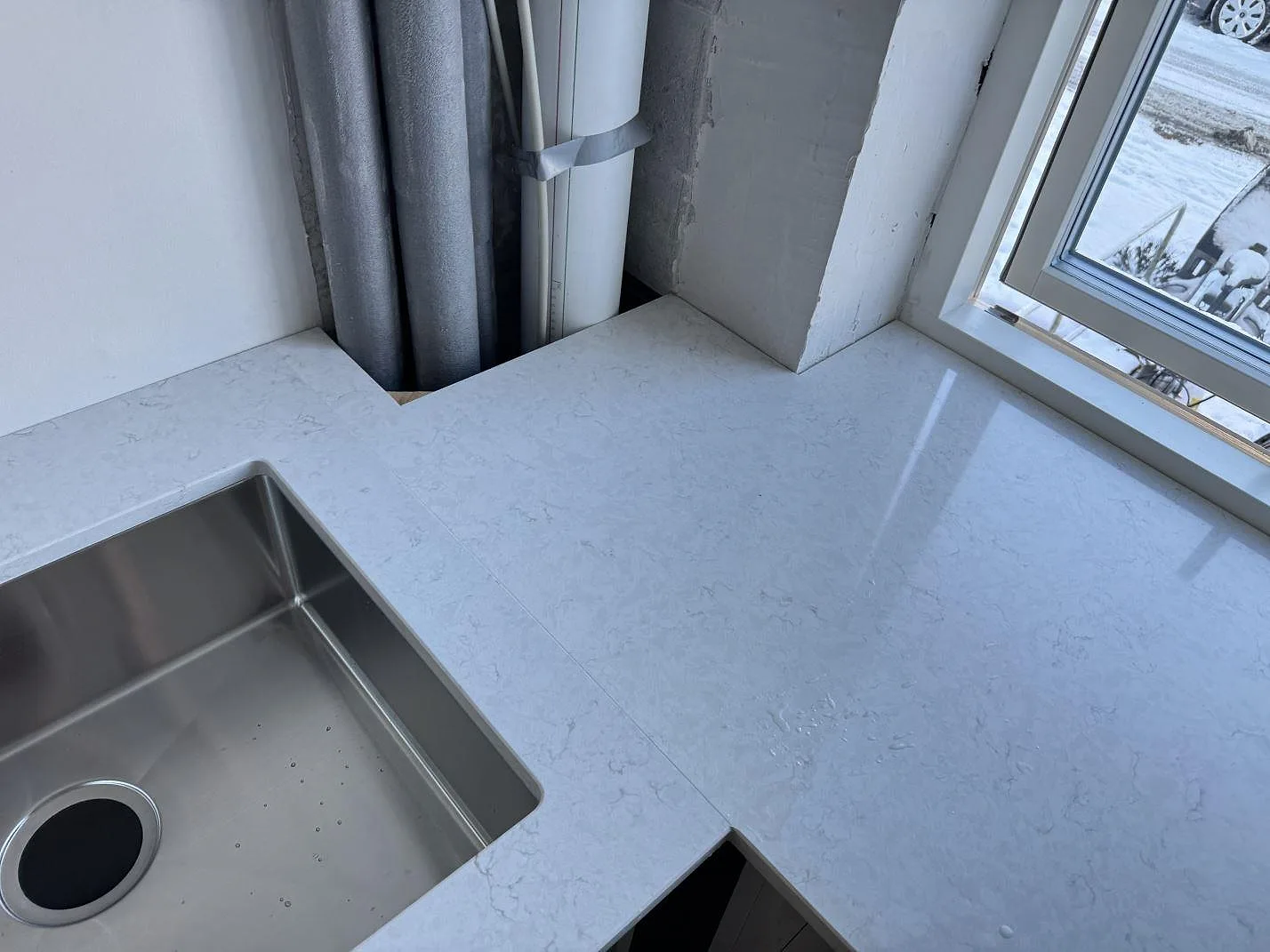 Ljus köksbänkskiva i Silestone Snowy Ibiza med rostfri diskho och blank ådrad yta vid fönstret i Bagsværd.