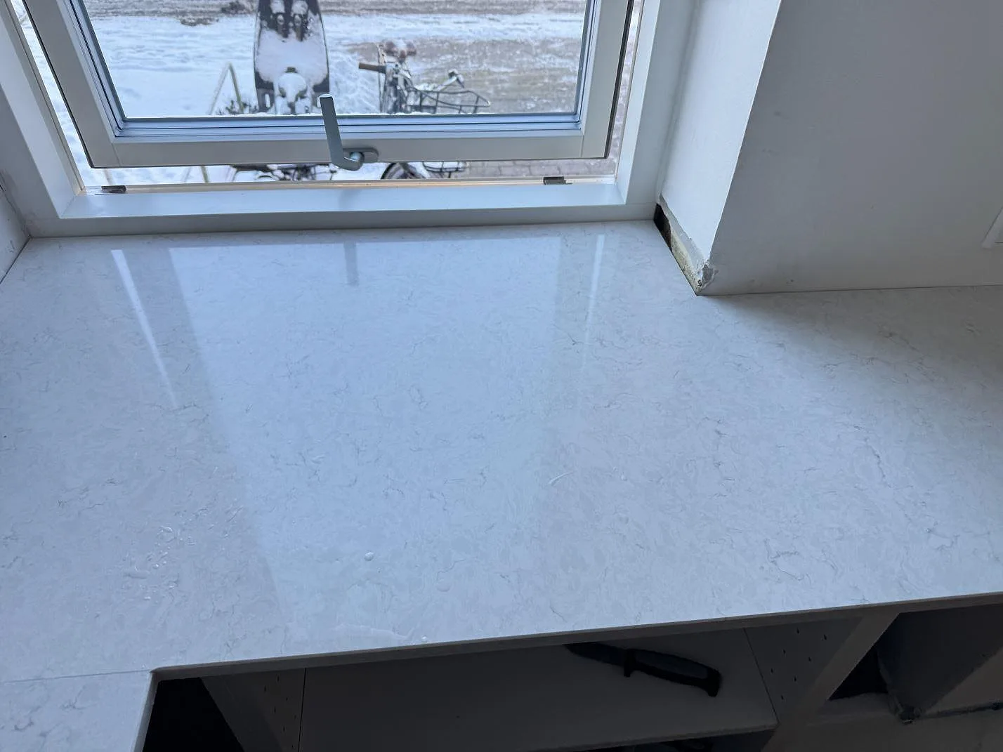 Blank vit Silestone Snowy Ibiza bänkskiva med grå ådring framför fönstret i ett kök under montering i Bagsværd.