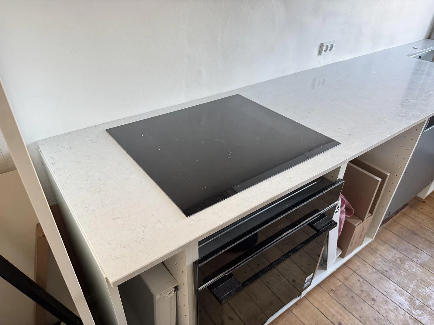 Polerad Silestone Snowy Ibiza köksbänkskiva med svart häll och ugn under arbetsytan i ett kök under montering i Bagsværd.