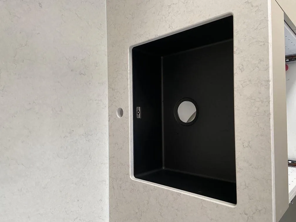 Underlimmad svart kompositdiskho i en polerad Silestone Snowy Ibiza bänkskiva i ett kök i Bara.
