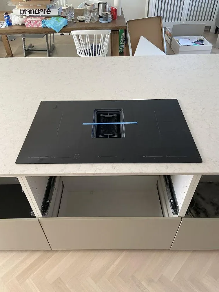 Köksbänkskiva och köksö i vit Silestone Snowy Ibiza, polerad, med en mörk häll i urtaget och öppna stommar under monteringen i ett kök i Bara.