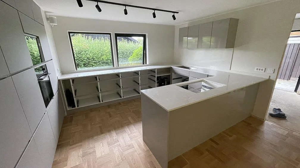 Polerad köksbänkskiva i Silestone Snowy Ibiza, vit kvartskomposit med 12 mm stänkskydd i ett kök under montering i Bjärred.