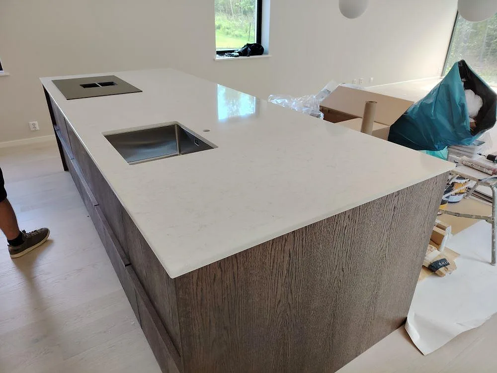 Köksö med bänkskiva i vit Silestone Snowy Ibiza, polerad kvartskomposit, underlimmad rostfri diskho och hällplats i ett kök i Bjursås.