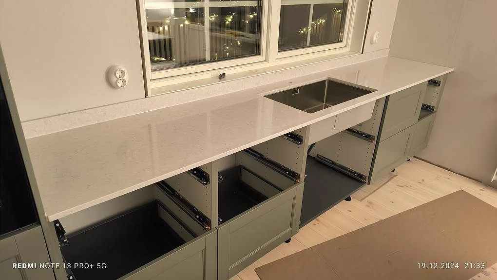Polerad Silestone Snowy Ibiza som bänkskiva och låg stänkdel vid fönster och synlig diskho i kök i Bjursås.