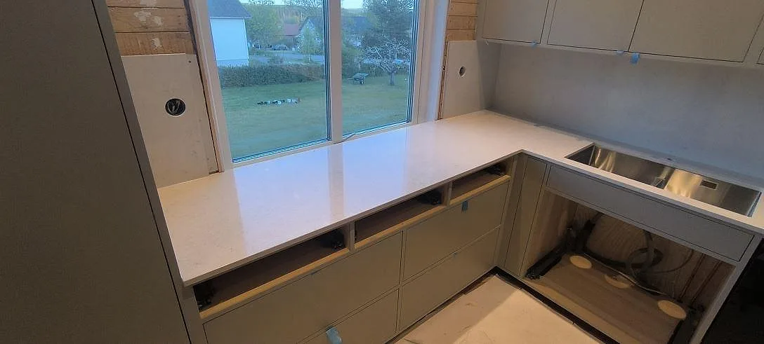 Fönstersidan i ett Bjursås-kök med polerad Silestone Snowy Ibiza som bänkskiva och stänkskydd vid diskhörnet.