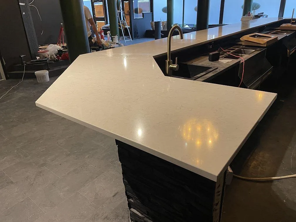 Lång bardisk i 20 mm polerad Silestone Snowy Ibiza komposit med mässingsfärgad blandare under montering i Borås.