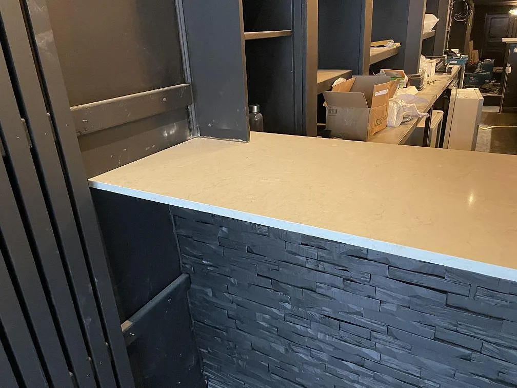 Ändstycke av bardisk i Silestone Snowy Ibiza komposit mot mörk inredning och hyllor under montering i Borås.