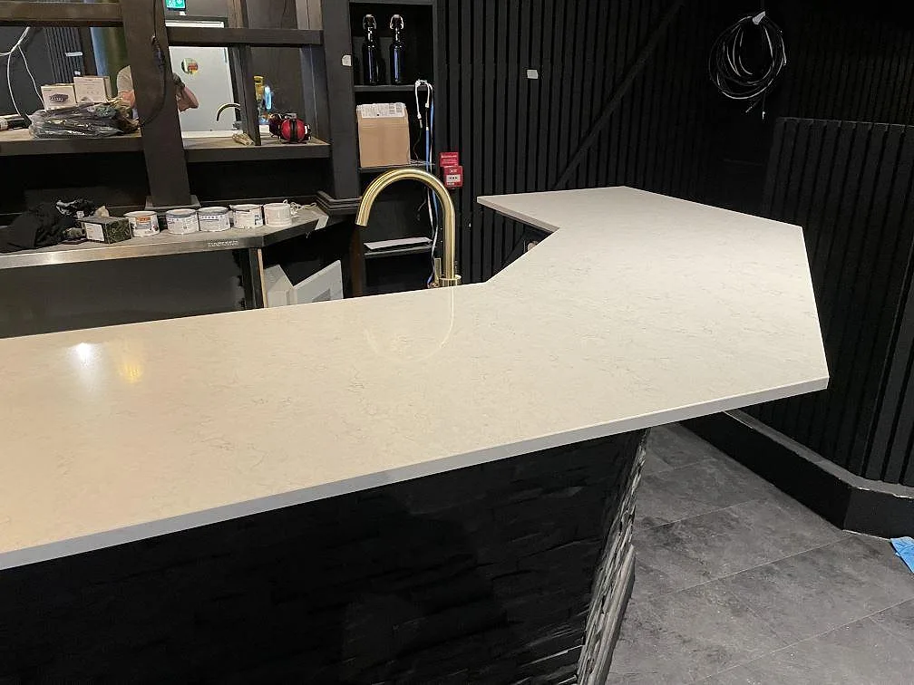 Närbild på polerad Silestone Snowy Ibiza som bardisk med mässingsfärgad blandare och svart väggpanel i Borås.
