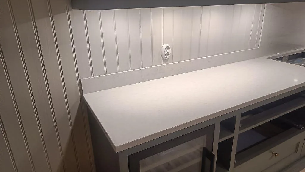 Lång arbetsyta i polerad Silestone Snowy Ibiza, vit kompositbänkskiva med uppvikt stänkkant under väggskåp i Braås.