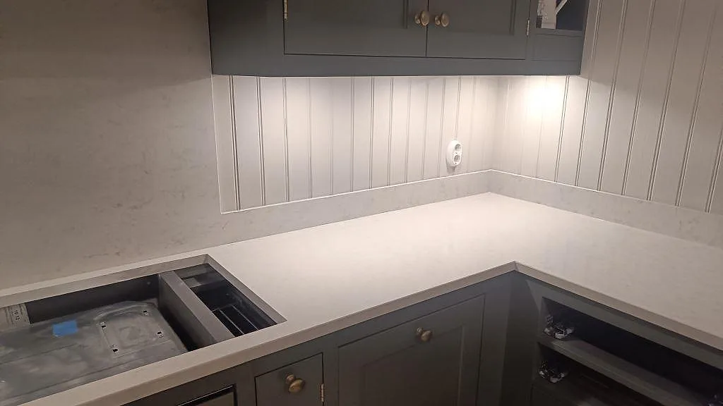 Polerad Silestone Snowy Ibiza som köksbänkskiva i hörn med låg stänkkant och grågröna köksluckor i Braås.