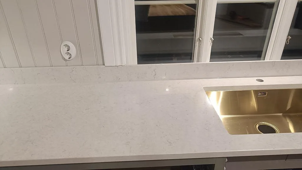 Detalj av polerad Silestone Snowy Ibiza i kök i Braås, med ljus ådring, uppvikt stänkkant och synlig vattenzon.
