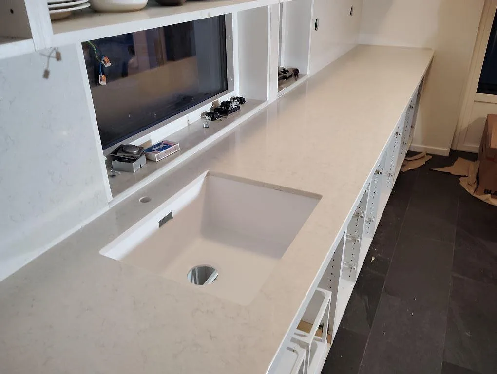 Köksbänkskiva i vit Silestone Snowy Ibiza, polerad kvartskomposit, med underlimmad diskho i ett kök under montering i Bro.