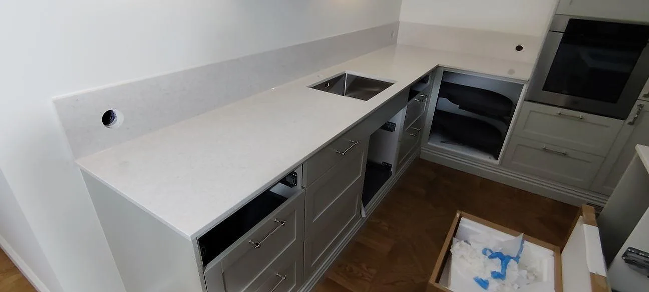 Väggbänk i polerad Silestone Snowy Ibiza med synlig diskho och uppvikt stänkkant under montering i Bromma.
