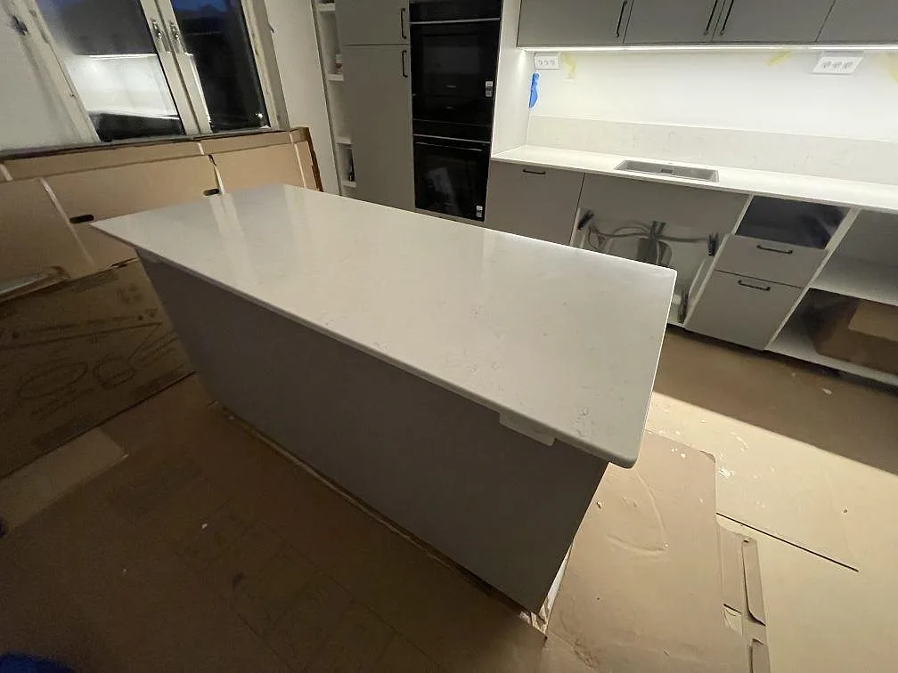 Närbild på polerad Silestone Snowy Ibiza på köksö i Bromma, med väggbänk, diskho och låg stänkkant i bakgrunden.