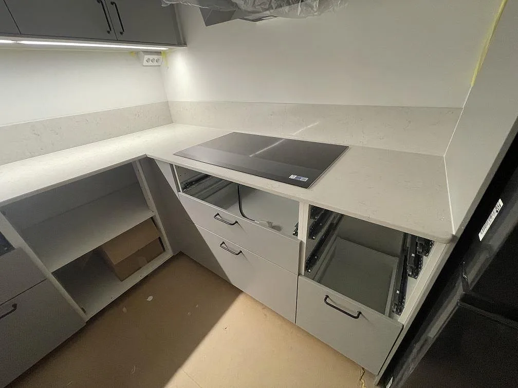 Polerad Silestone Snowy Ibiza som köksbänkskiva med synlig induktionshäll, låg stänkkant och grå köksinredning i Bromma.