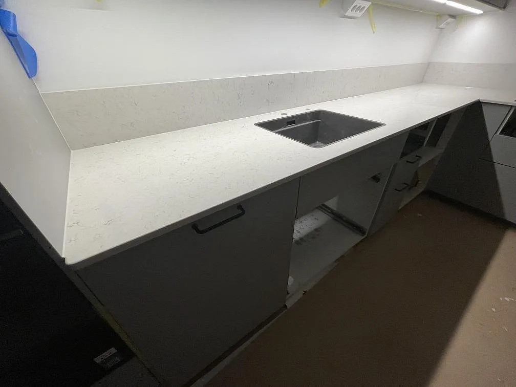 Polerad köksbänkskiva i Silestone Snowy Ibiza med låg stänkkant och synlig diskho i ett kök i Bromma under montering.