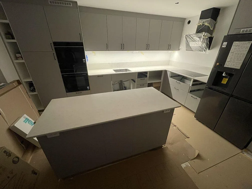 Kök i Bromma med polerad Silestone Snowy Ibiza som köksbänkskiva, låg stänkkant, köksö, synlig diskho och häll under montering.