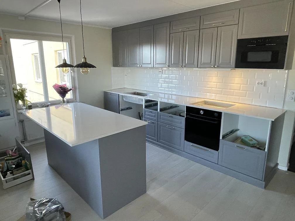Vit köksbänkskiva och köksö i polerad Silestone Snowy Ibiza i ett kök med grå luckor och vitt tegelkaklat stänkskydd i Bromma, fotograferat under montering.