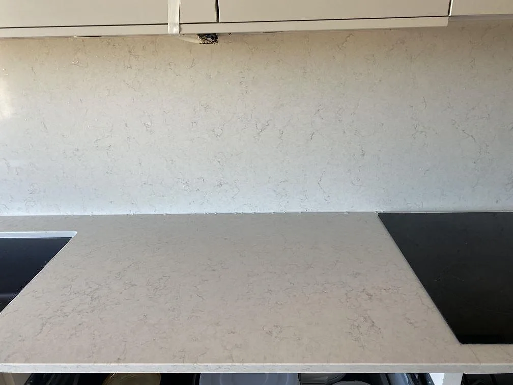Polerad Silestone Snowy Ibiza köksbänk med heltäckande väggbeklädnad i samma kvartskomposit, diskho till vänster och induktionshäll till höger, i ett kök i Bunkeflostrand.