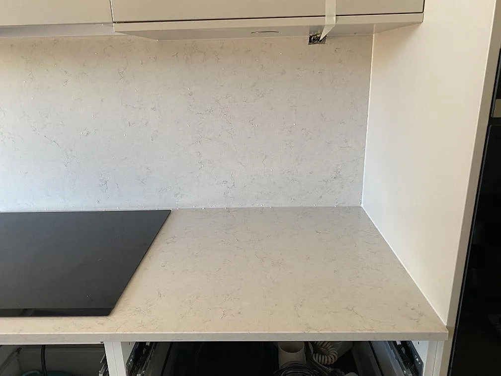 Detalj av Silestone Snowy Ibiza vid induktionshällen med heltäckande väggbeklädnad och fin grå ådring i ett kök i Bunkeflostrand.