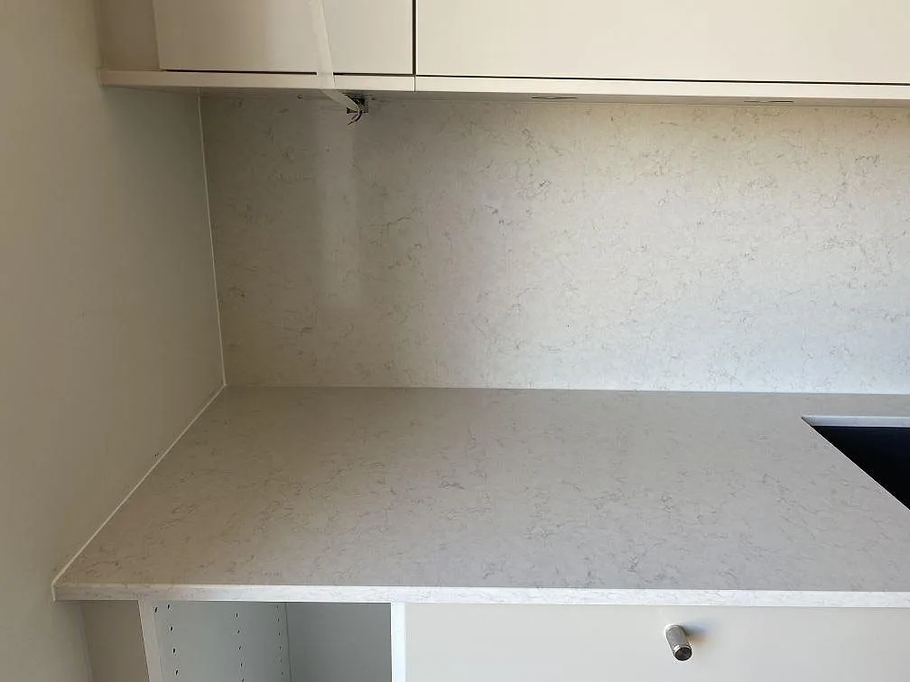 Hörn av köksbänken i Silestone Snowy Ibiza med heltäckande väggbeklädnad i samma sten mot ljusa greppfria köksluckor i Bunkeflostrand.