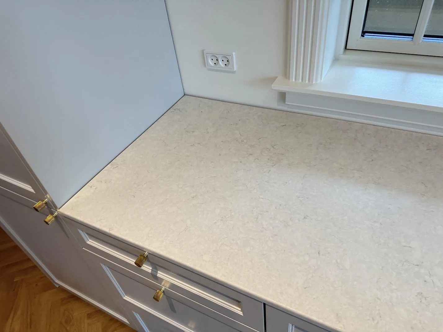 Hörnvy av köksbänkskiva i matt Silestone Snowy Ibiza med fönsterljus och mässingsfärgade beslag i Charlottenlund.