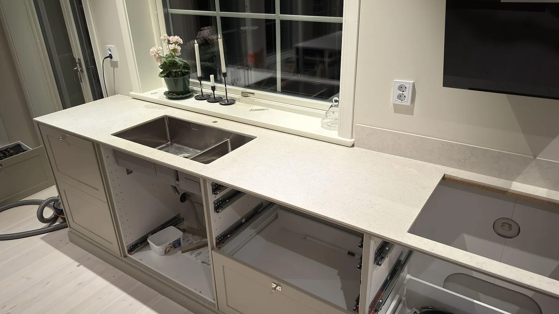 Underlimmad rostfri diskho och infälld induktionshäll i matt Silestone Snowy Ibiza längs fönsterväggen i ett kök i Dala Floda.