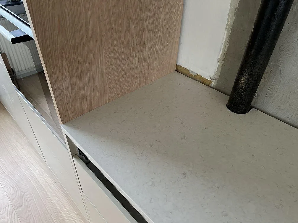 Detalj av polerad Silestone Snowy Ibiza på vit köksstomme intill träinredning och rördragning i Dalby.