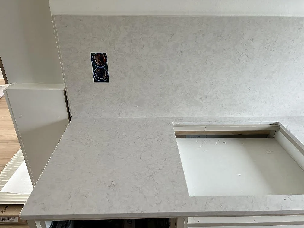 Polerad köksbänkskiva i Silestone Snowy Ibiza med utskuren hällöppning och stänkskydd under montering i Dalby.