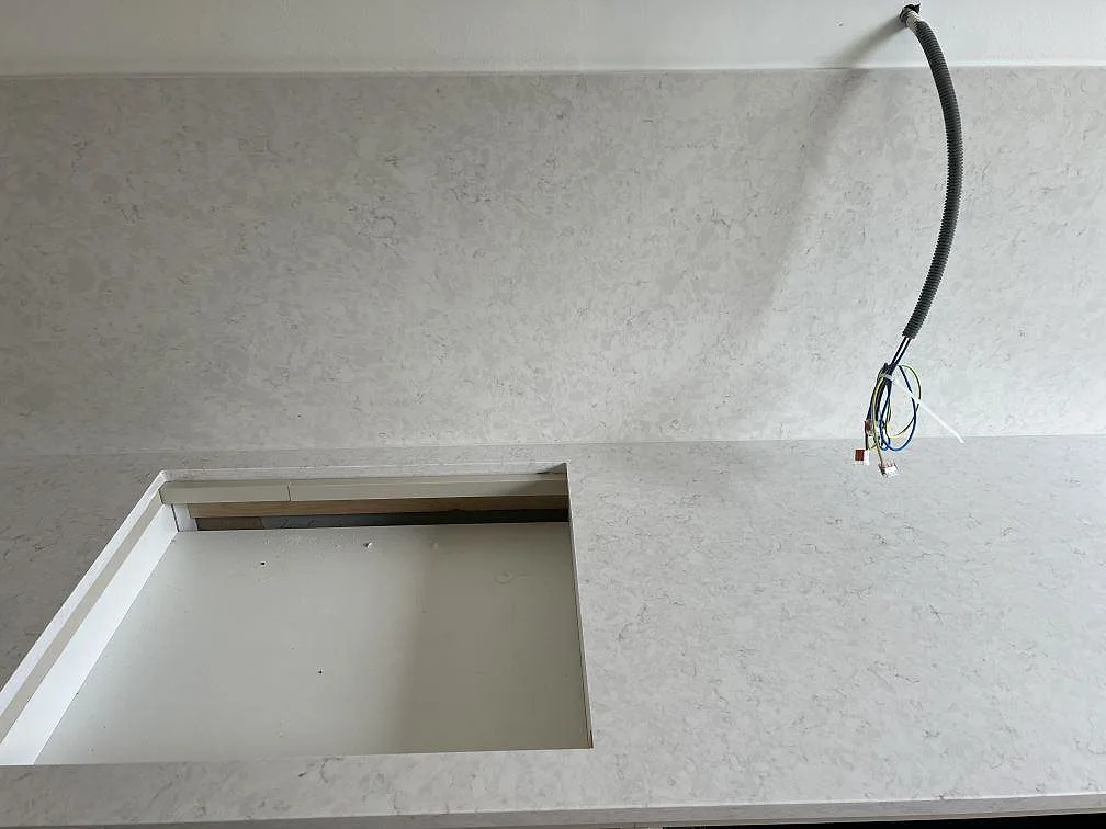 Ljus Silestone Snowy Ibiza i polerad komposit med hällöppning, kabeldragning och stänkskydd i ett kök i Dalby.