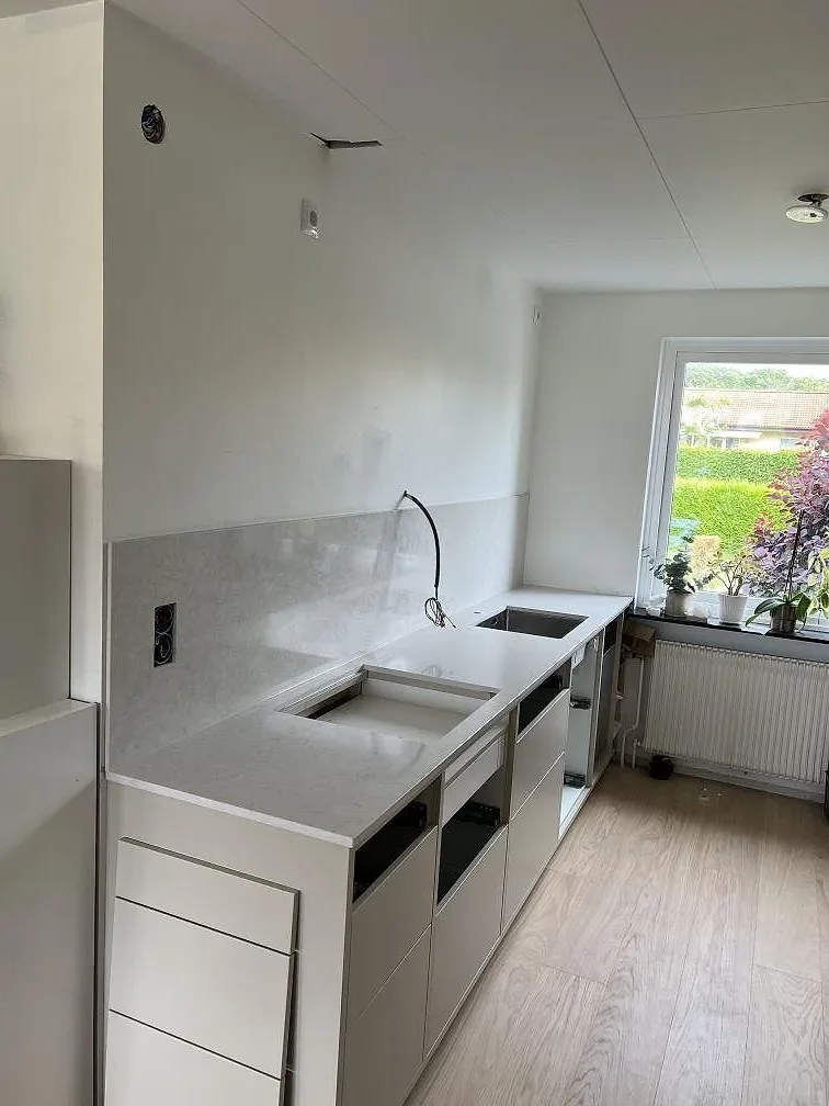 Översiktsbild av kök i Dalby under montering med polerad Silestone Snowy Ibiza, hällöppning, diskho och vita stommar.