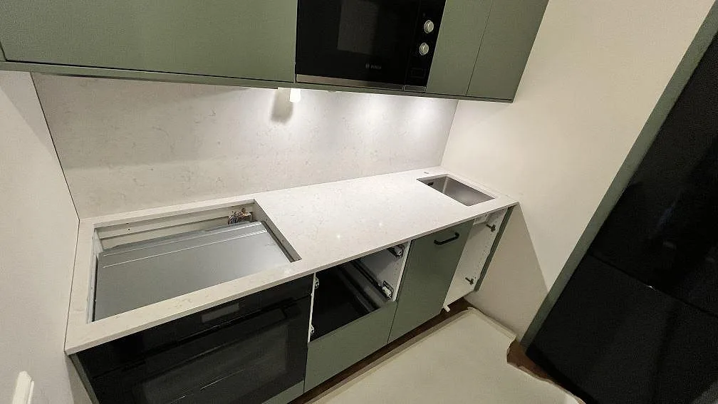 Rak köksbänkskiva i polerad Silestone Snowy Ibiza med hällurtag till vänster, rostfri diskho till höger och stänkskydd i ett kök i Danderyd.