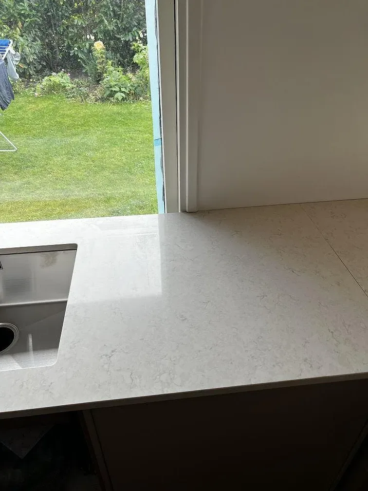 Närbild på polerad Silestone Snowy Ibiza runt rostfri diskho och blandarhål i kök i Dyssegård.
